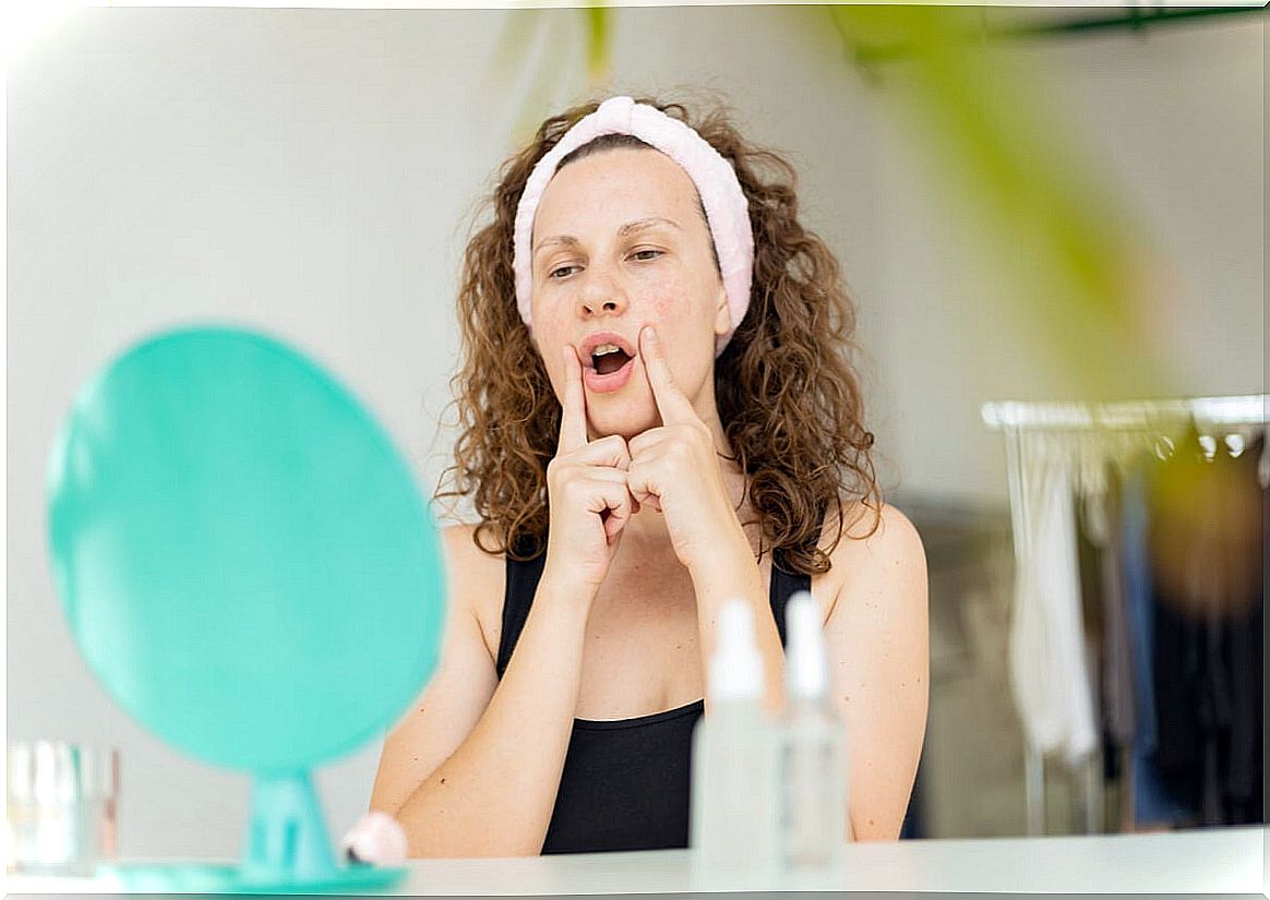 Woman performs facial yoga in front of a mirror.