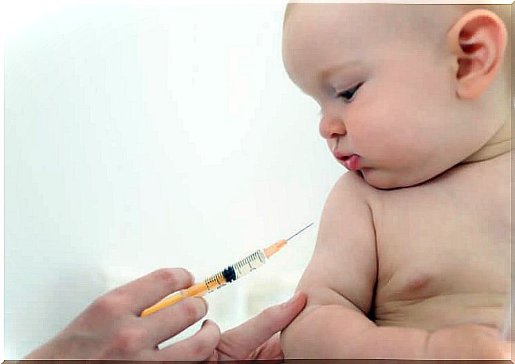 Baby watches an injection while holding his arm to be vaccinated.